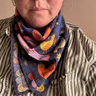 Person wearing a colorful bandana neck scarf with birds and chickens on a neutral background