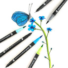 Brush tip pens and fine liner pens next to an illustration of a blue butterfly sitting on blue flowers with green stems