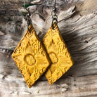 Boho earrings western aesthetic hand tooled yellow leather in a diamond shape dangle style on a wooden surface