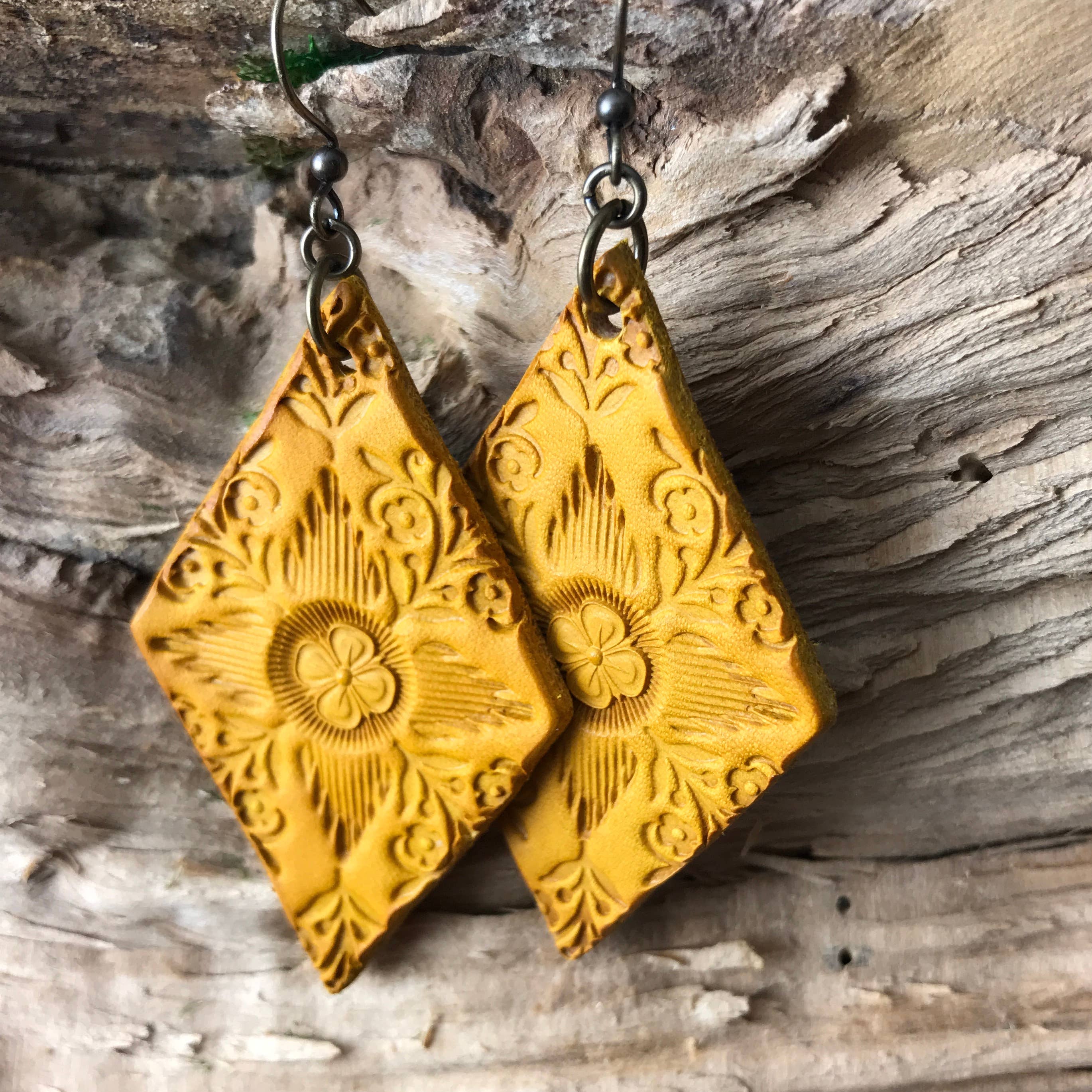 Boho earrings western aesthetic hand tooled yellow leather in a diamond shape dangle style on a wooden surface