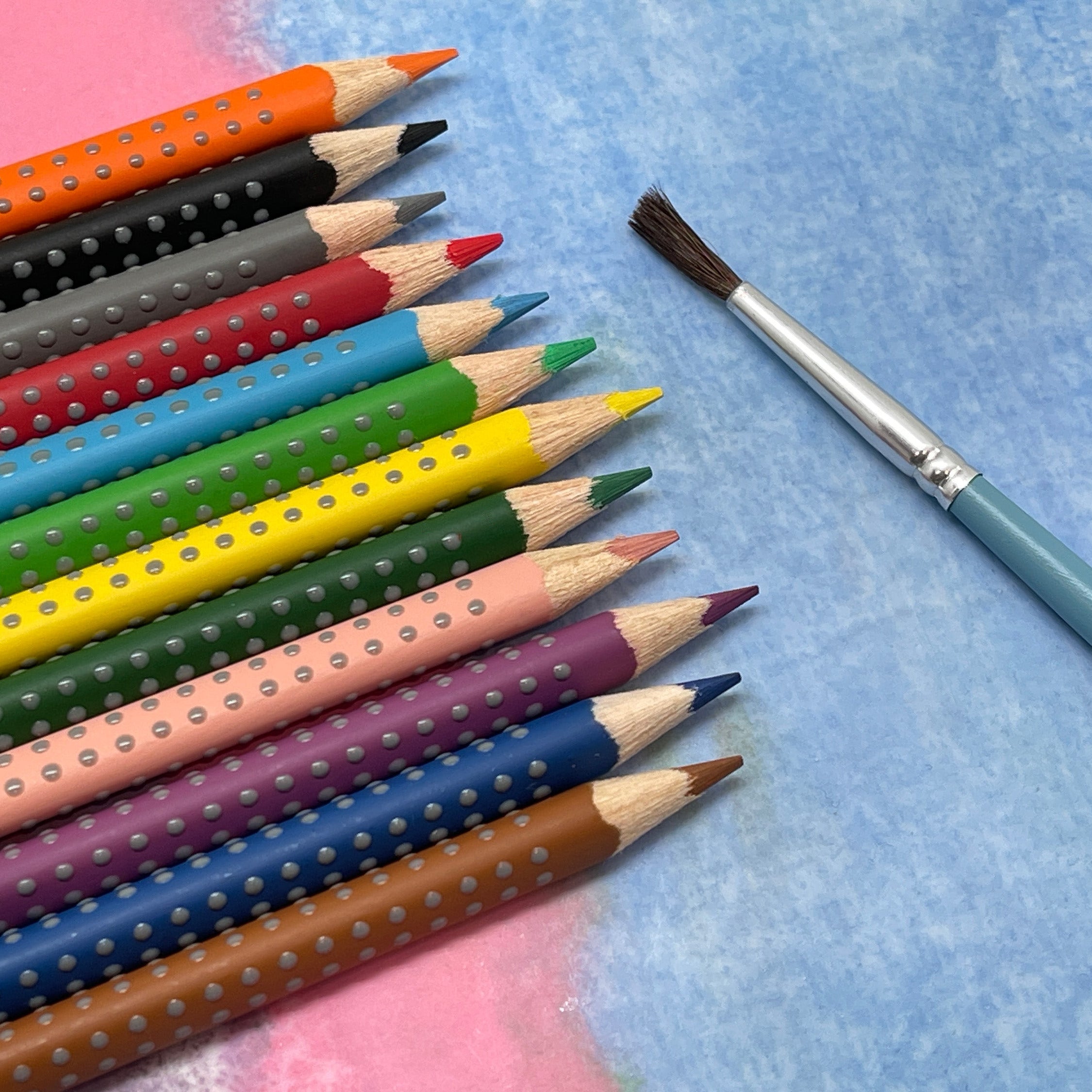Set of watercolor pencils with grip dots with a paintbrush on a textured surface