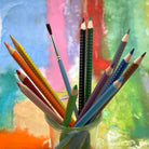 Colorful watercolor pencils and a paintbrush in a glass jar against a colorful abstract background
