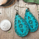 Turquoise patterned earrings on a wooden surface with a quarter for scale.