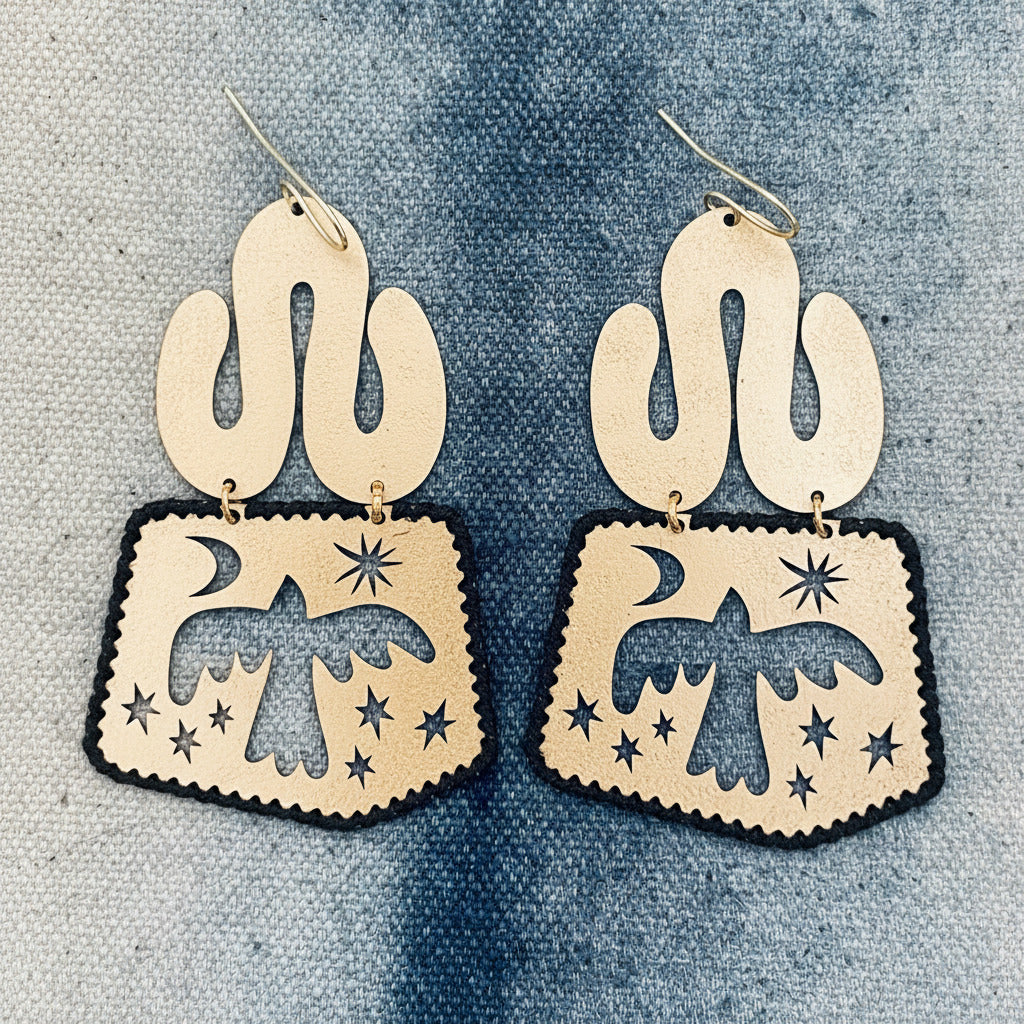 Pair of gold-tone brass boho style dangle earrings with cut-out designs of birds and celestial elements on a denim background