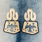 Pair of gold-tone brass boho style dangle earrings with cut-out designs of birds and celestial elements on a denim background