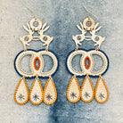 Pair of handmade brass dangle earrings in boho chic style with intricate designs of two hares dancing and hand stitched thread edges on a textured fabric background