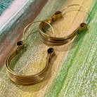Close up details of pair of hoop earrings made from brass on a muted color background