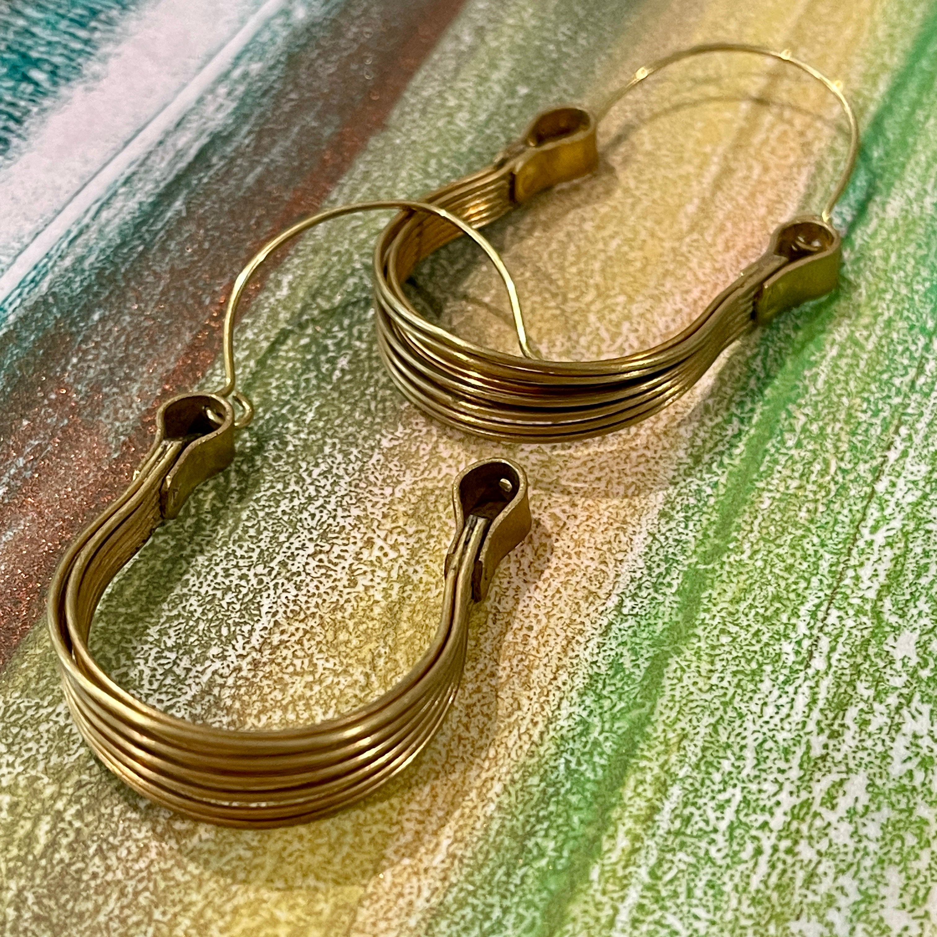Close up details of pair of hoop earrings made from brass on a muted color background