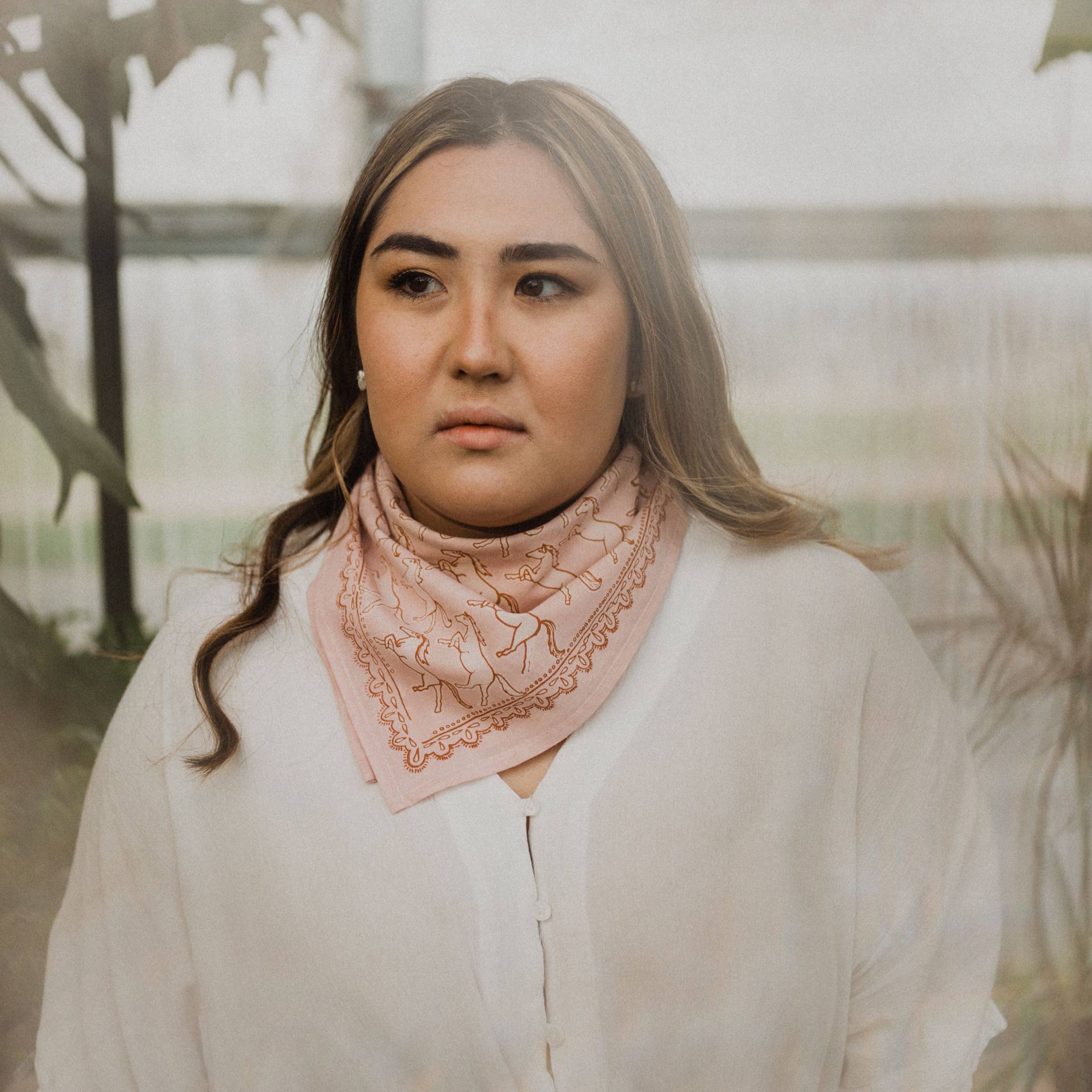 Woman wearing a pink scarf with horses pattern and a blurred outdoor background