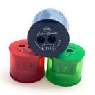 Three translucent plastic pencil sharpener cylinders in red, green, and blue, arranged together on a white background. The top sharpener is dark blue and displays the brand 'KUM' and model 'Color-Combi'.
