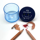 A KUM Color-Coni pencil sharpener set shown on a white background, including a transparent blue cylindrical container, a dark blue circular sharpening head with white printed branding, two wooden pencils, and shavings of wood and red pencil lead.