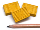 Three yellow KUM erasers with a pencil on a white background