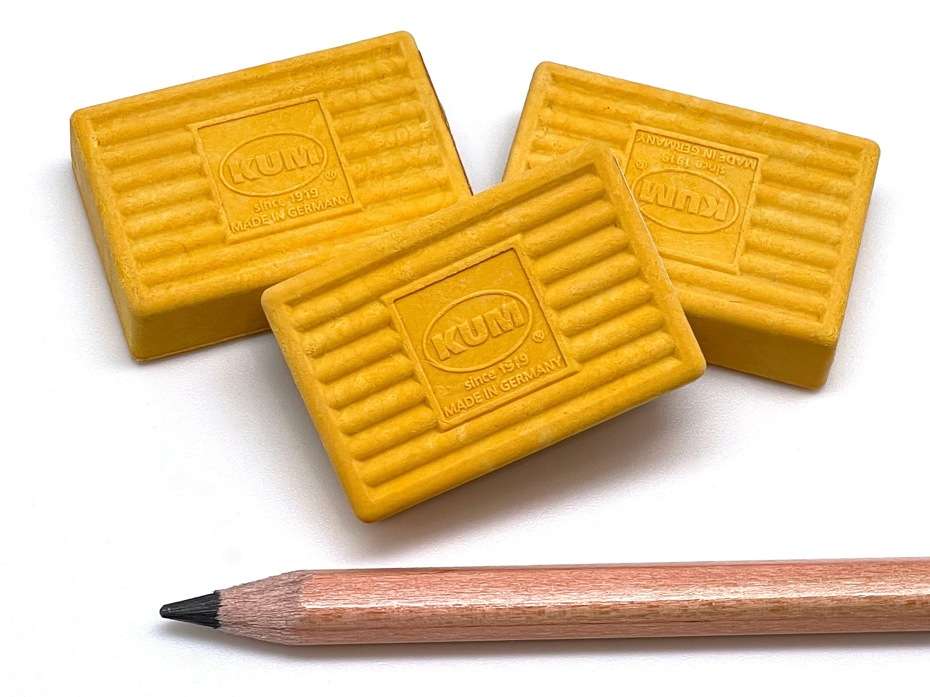 Three yellow KUM erasers with a pencil on a white background
