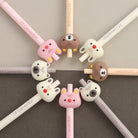 Cute and colorful pen tops with bunny and bear designs arranged in a circle on a muted background