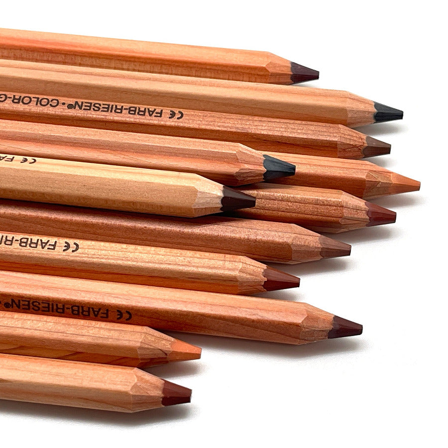 A close-up, diagonal arrangement of Lyra Color Giants colored pencils in various skin tones, including brown, beige, and muted red, on a clean white background.