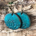 Pair of blue hand tooled leather earrings with mandala pattern on a wooden surface