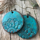 Turquoise mandala earrings on a wooden surface with feathers and flowers.