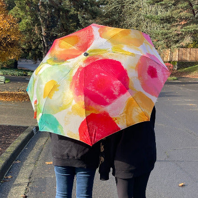 Two people standing outside on an autumn day under a colorful umbrella made from an original art painting 