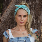 Woman artist wearing cotton bandana  headband and denim overalls standing against a tree.