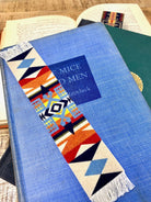 Colorful geometric Pendleton blanket pattern bookmark on a blue book with 'Of Mice and Men' visible