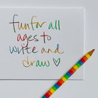 A white square card with colorful handwritten text reading 'fun for all ages to write and draw' and a small heart, shown on a white background with a rainbow-striped pencil placed diagonally across the lower right corner.