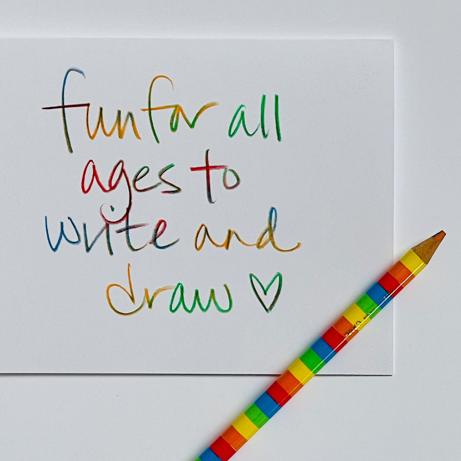 A white square card with colorful handwritten text reading 'fun for all ages to write and draw' and a small heart, shown on a white background with a rainbow-striped pencil placed diagonally across the lower right corner.