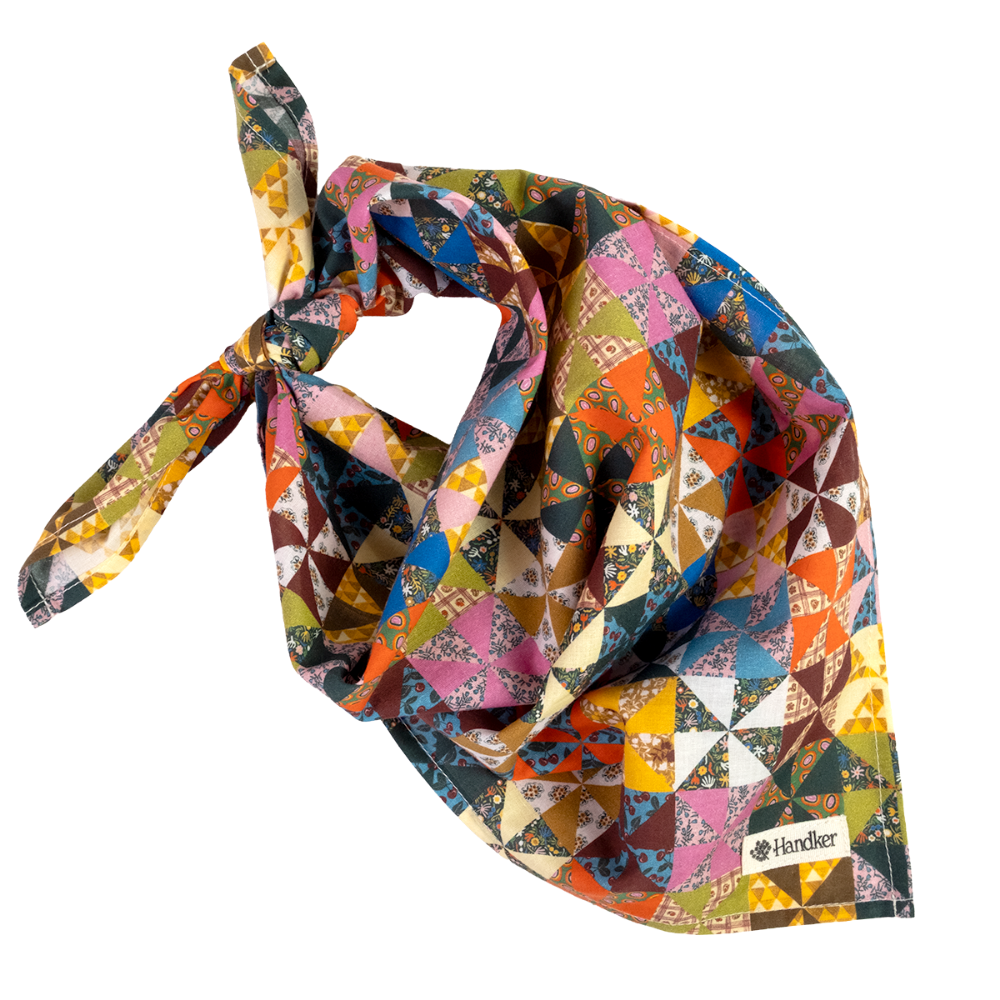 A multicolor Calico geometric-patterned bandana tied in a knot, featuring a patchwork design of triangles and squares in orange, blue, pink, yellow, green, and brown. A small white brand label reading 'Handker' is visible in the bottom right corner, set against a clean white background.