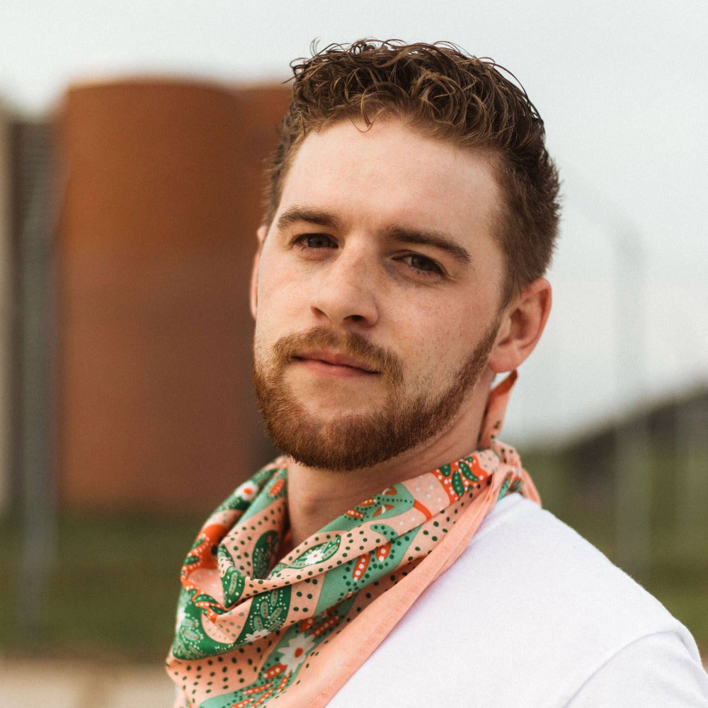 Man wearing a colorful scarf cotton bandana with a blurred outdoor background