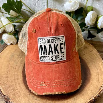 Orange distressed cap with a black and white patch on a wooden surface with flowers in the background