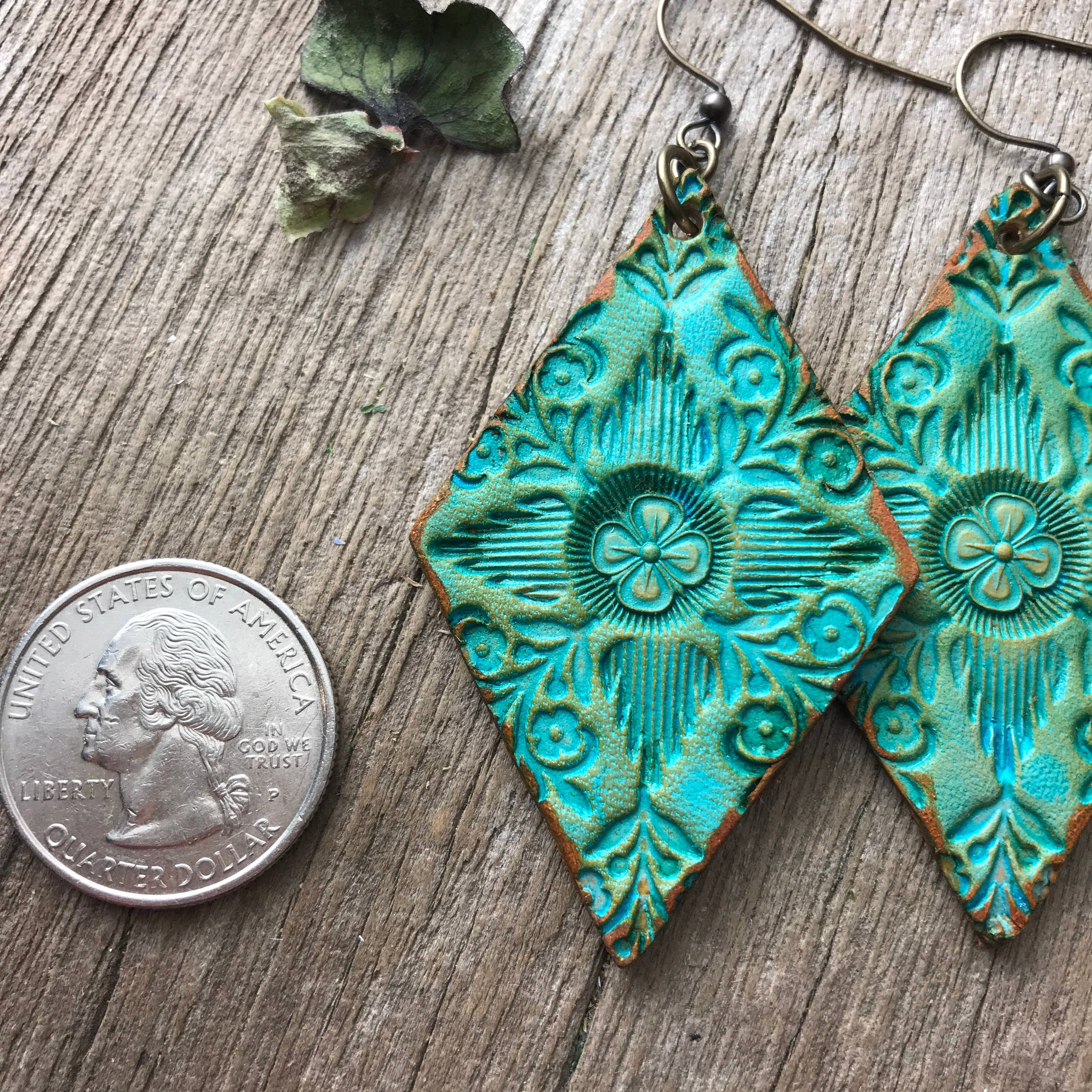 Turquoise hand tooled leather dangle earrings on a wooden surface with a quarter for scale.