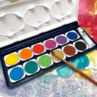 Watercolor paint box with 12 colors of paint and a paint brush against a colorful background