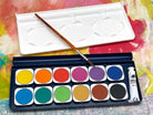 Watercolor paint set with brush and lid on a colorful background