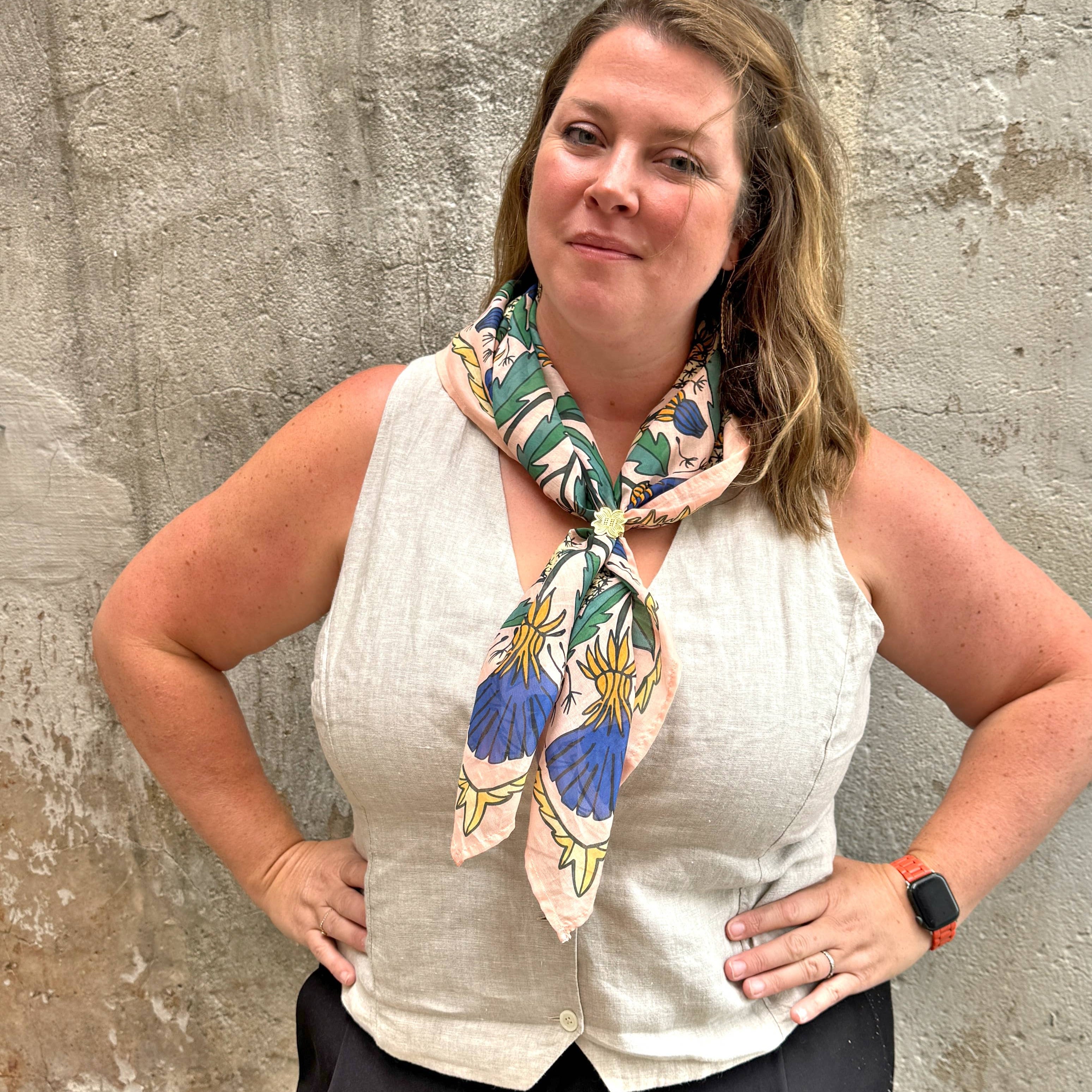 Woman wearing a wild rag bandana scarf, white top, and black pants against a textured wall.