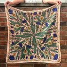 Person holding a square dandelion patterned wild rag scarf against a brick wall