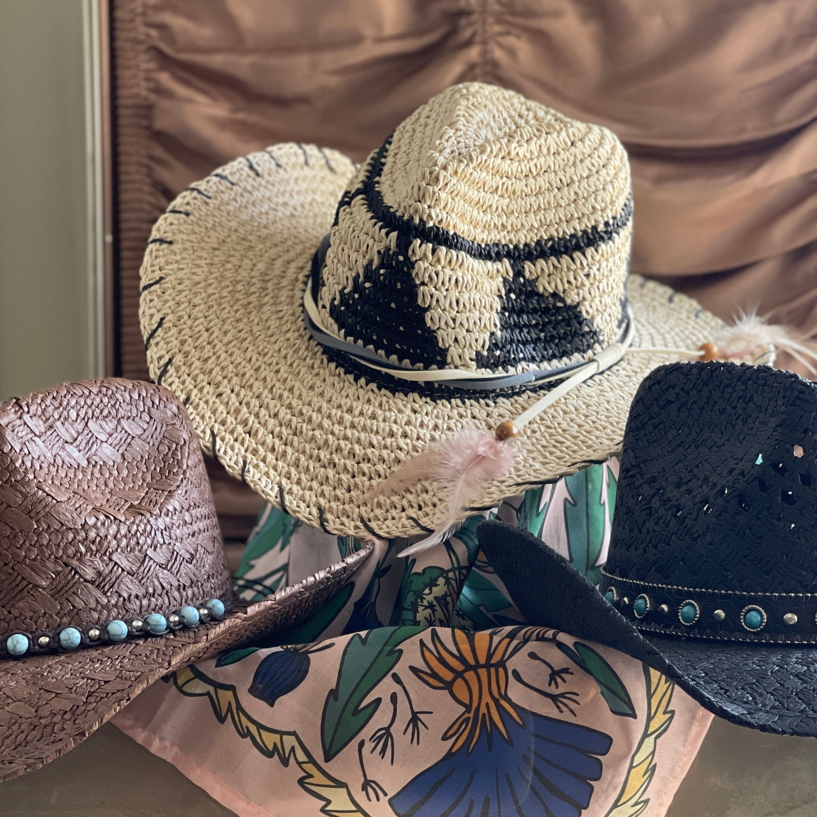 Woven straw hats stacked on display with a pink fabric scarf and muted background