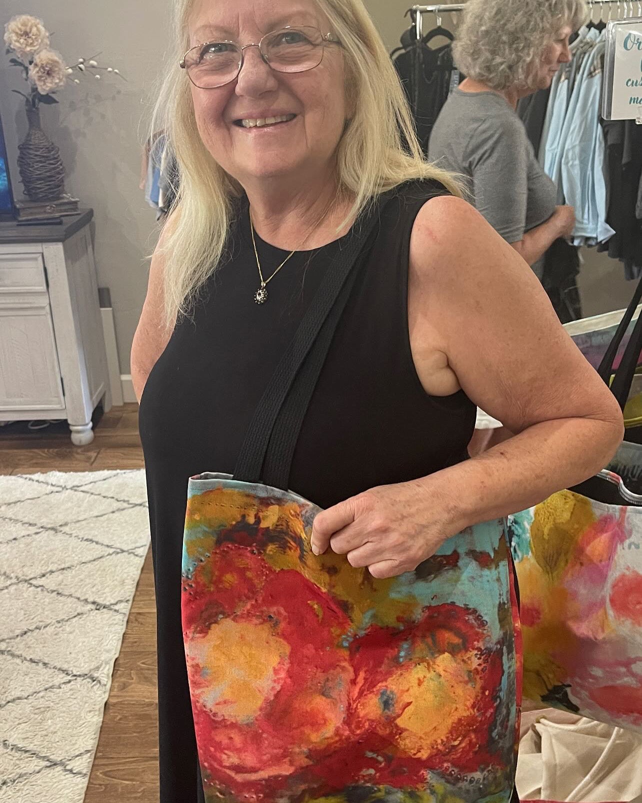 Woman holding a colorful shoulder tote bag featuring a floral painting in a casual indoor setting