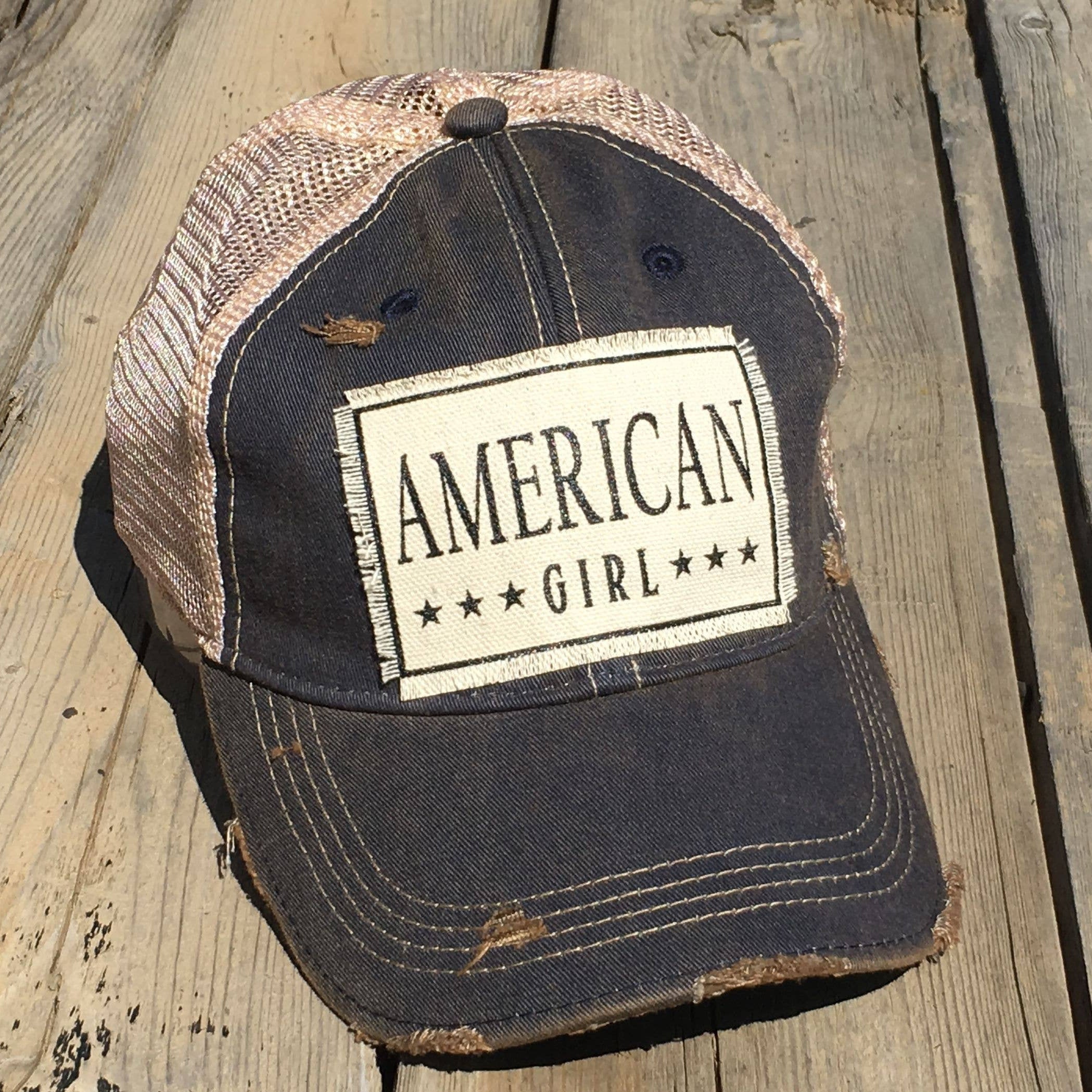 Navy blue and beige cap with 'American Girl' patch on a wooden surface