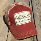 Red and brown cap with 'American Girl' logo on a wooden surface