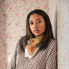 Woman wearing a checkered shirt with a floral patterned cotton bandana scarf against a floral wallpaper background