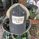 Denim cap with 'Country Girl' logo on a plant stand with plants in the background