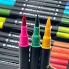 Pink, green and yellow brush pens with colorful markers in a set in the background