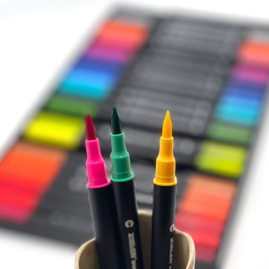 three brush pens (pink, green, yellow) close up view with the blurred set of duo tip pens in the background