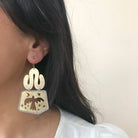 Close up of handmade earring made of brass with a bird design on a neutral background