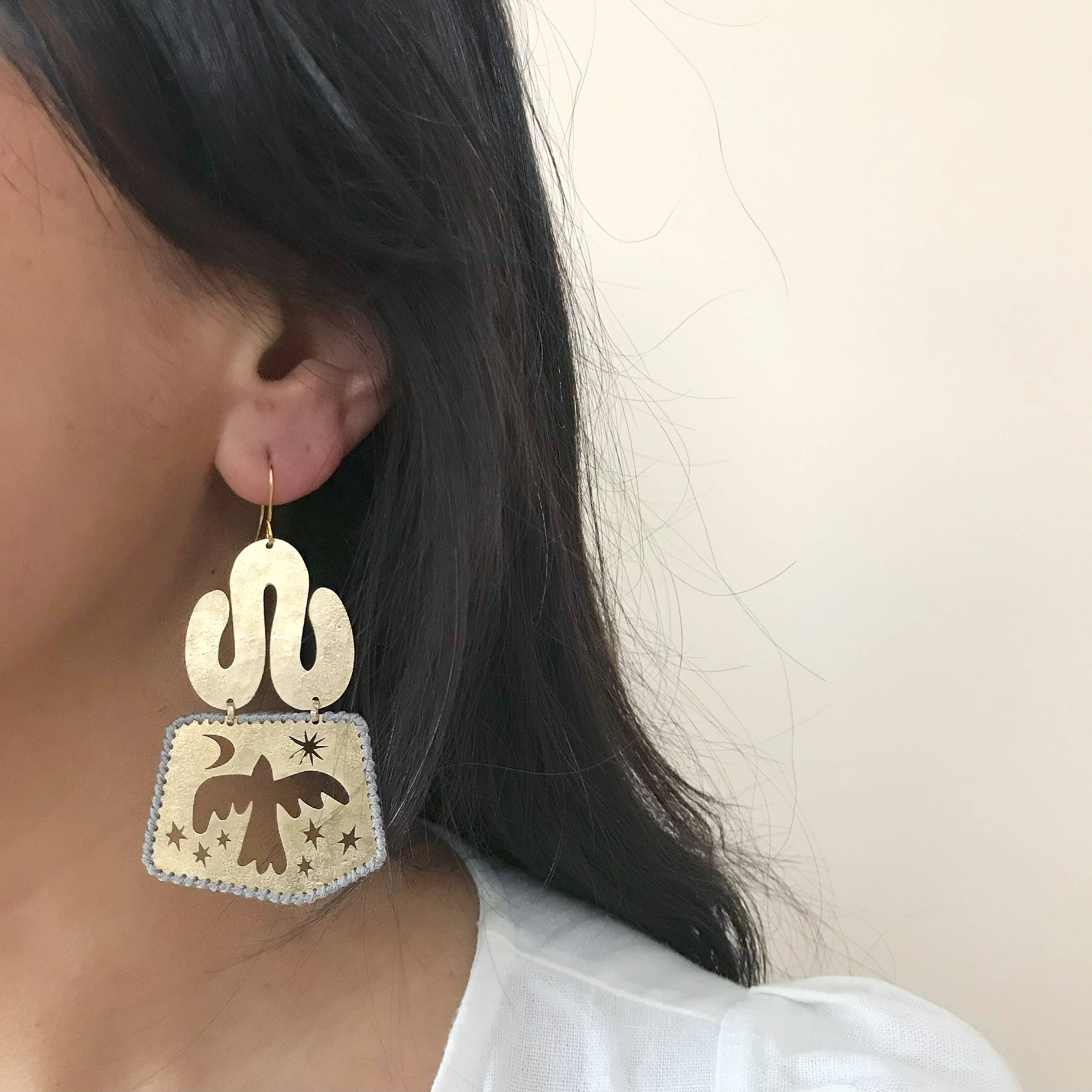Close up of handmade earring made of brass with a bird design on a neutral background