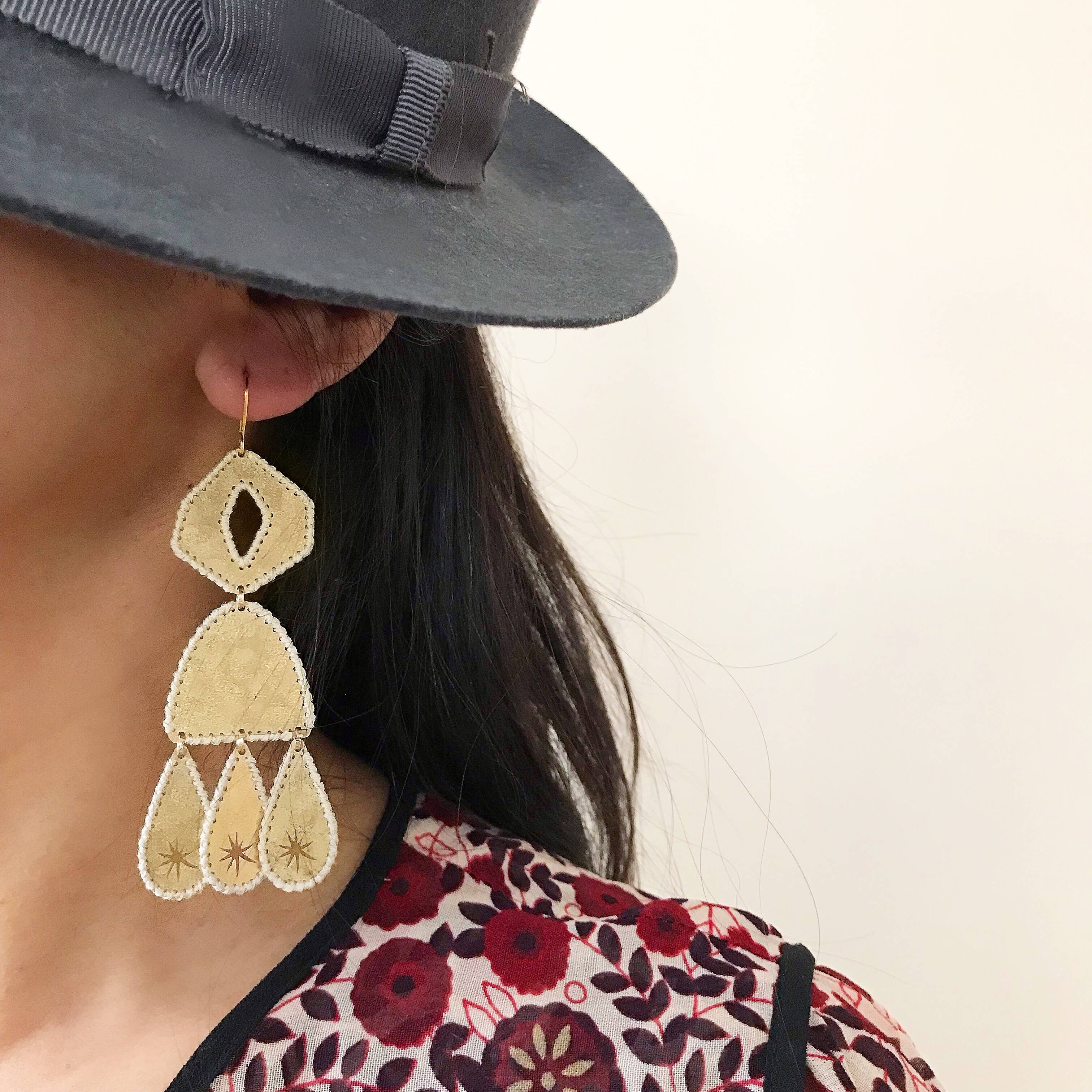 Close-up of a person wearing a gray hat and gold-tone handmade earrings with a floral-patterned garment.