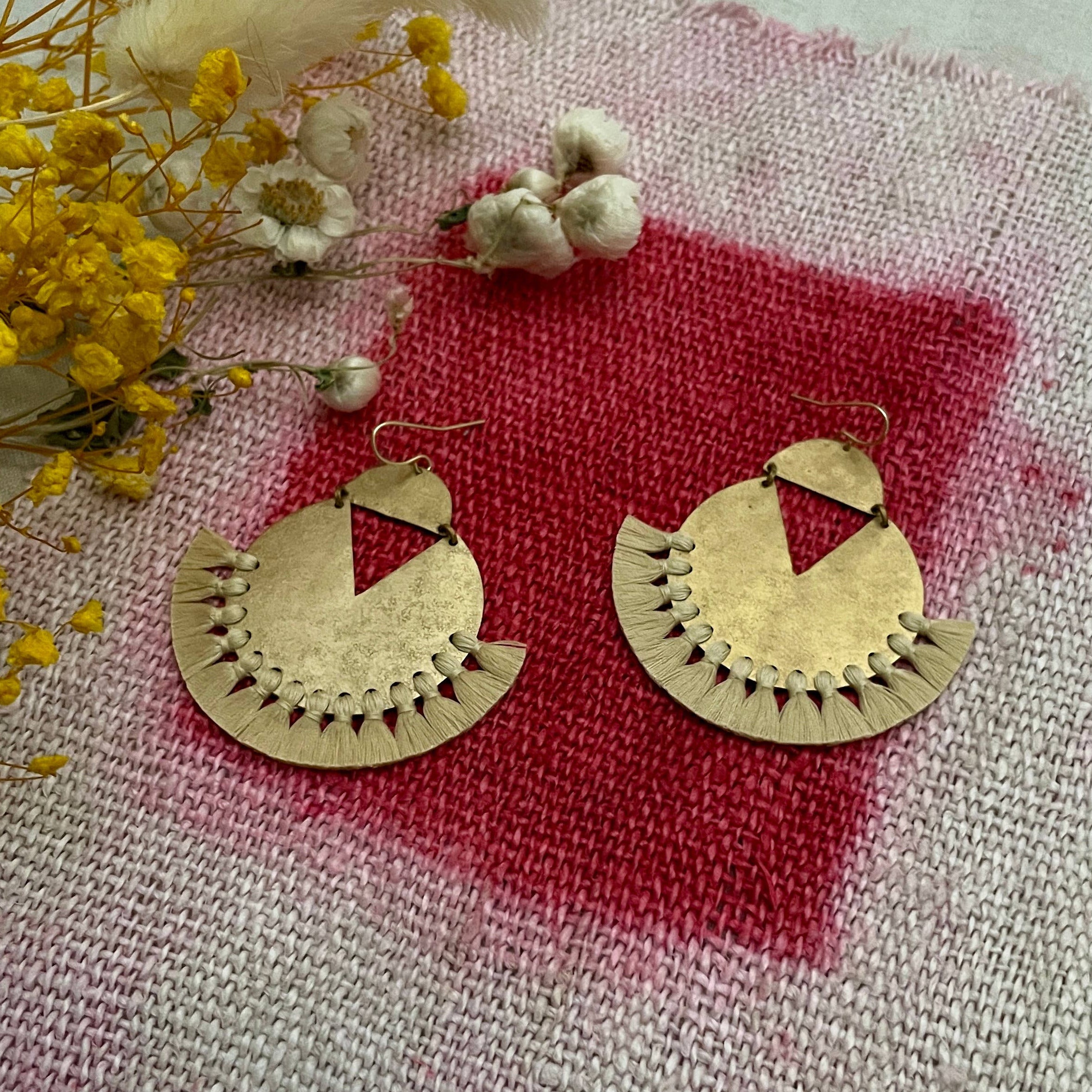 Gold earrings on a textured fabric surface with yellow flowers.