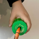 Child hand holding a green wax crayon sharpener and an orange jumbo crayon against a cream background