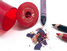 A red jumbo crayon sharpener container, sharpened crayon pieces, jumbo pencils sharpened and a purple crayon on a white background.