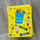stack of yellow sketchbooks with colorful crayon illustrations on a wooden surface
