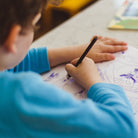 Child drawing with a pencil in a sketchbook at a table. Screen free activity for kids